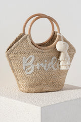 Carry something borrowed and something blue in Shiraleah's "Bride" Mini Tote. The elegant beaded script design and ivory tassle and pom details make it perfect accessory for your bridal excursions. Made from woven jute with a chic circular top handle, this bag can be carried effortlessly throughout your honeymoon or bachelorette! Pair with other items from Shiraleah's Hitched collection to complete your special day's look!