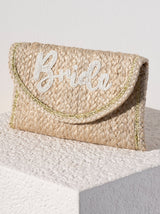 A flat, rectangular clutch purse made of woven natural material with the word "Bride" embroidered in white beads and a gold lurex hem