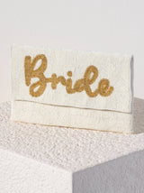 A flat, rectangular clutch purse embroidered all over with white beads and the word "Bride" embroidered in gold beads