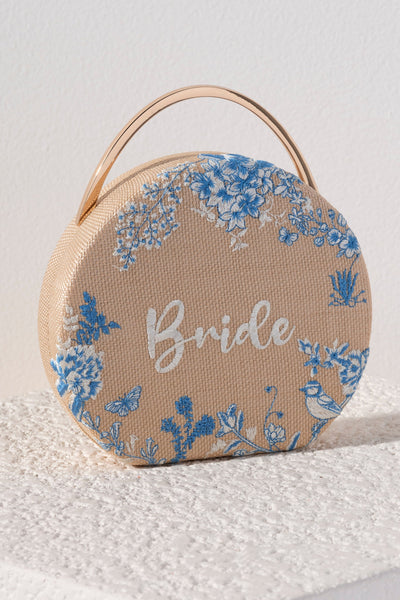 Bring your bridal celebrations wherever you go with Shiraleah's "Bride" Round Top Handle Bag. This chic circular bag features a sturdy top handle and an elegantly embroidered design. The word "Bride" is stitched in white letters with delicate blue florals around it. Pair with other items from Shiraleah's Hitched collection to complete your look!
