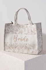 Carry all your essentials in style with Shiraleah's "Bride" Tote. This soft but structured canvas bag is elegantly designed with a beige floral background and the word "Bride" stitched neatly across the front. Pair with other items from Shiraleah's Hitched collection to complete your look!
