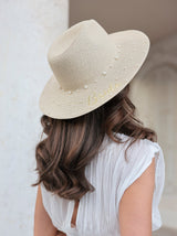 A model faces away from the camera to show a naturally colored woven hat with faux pearl embroidery and the word "Bride" in gold lurex